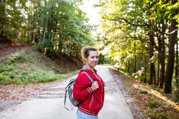 Beautiful woman smiling at path in a forest during hiking on a hill during sunrise on summer