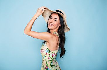 Naklejka premium Portrait of cute summer brunette woman in hat and colorful dress, stylish girl have a fun and posing on blue background