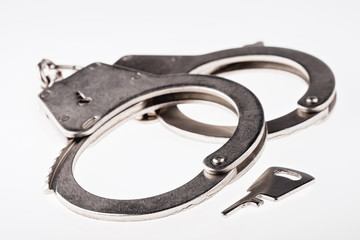 Pair of handcuffs and key on white background. This is usually done to prevent suspected criminals from escaping police custody.