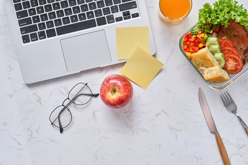 Top view of laptop, orange juice in glass and fresh salad in lunch box  at workplace