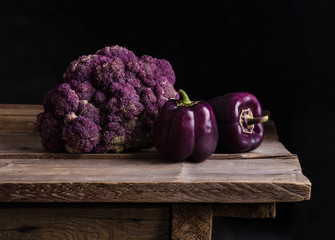 Fresh vegetable. Dark purple peppers and cauliflower on old rustic wooden table on black background