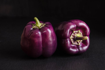Fresh vegetable. Dark purple peppers on black stone, black background