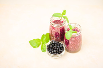 Blueberry smoothie decorated with fresh green mint leaves and raw ripe berries on yellow pastel background.