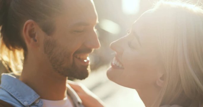 Happy smiled Caucasian young couple hugging and caressing while standing in sunlight. Outdoors.