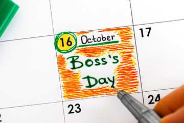 Woman fingers with pen writing reminder Boss`s Day in calendar.