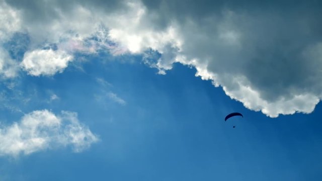 Tandem paragliders flying in the blue dramatic sky with clouds and sun rays