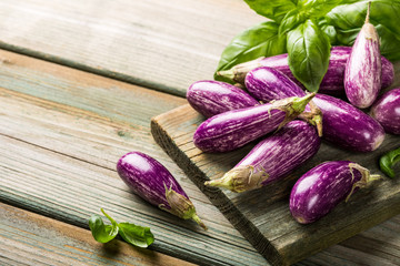 Heap of small eggplant or aubergine vegetable with basil leaves on old wooden background. Healthy food concept with copy space.