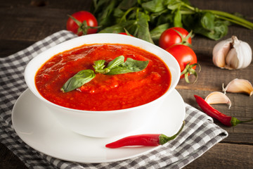 Fresh, healthy tomato soup with basil, pepper, garlic, tomatoes and bread on wooden background. Spanish gazpacho soup.