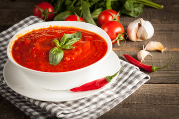 Fresh, healthy tomato soup with basil, pepper, garlic, tomatoes and bread on wooden background. Spanish gazpacho soup.