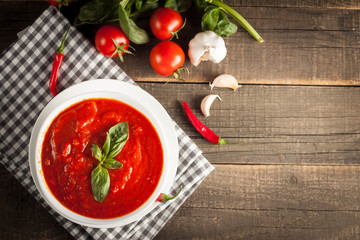 Fresh, healthy tomato soup with basil, pepper, garlic, tomatoes and bread on wooden background. Spanish gazpacho soup.