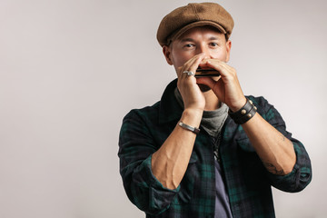 Caucasian maustached male traveler, wearing trendy cap playing a harmonica and looking at camera, isolated over white background. Travel lifestyle concept - obrazy, fototapety, plakaty