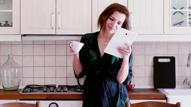 Beautiful, young woman sitting in bathrobe with tablet in the kitchen
