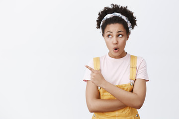 Surprised and amazed good-looking teenage girl with dark skin and curly hair in headband and yellow...