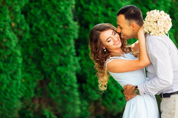 Naklejka premium the guy gently kisses his girlfriend who closed her eyes and bend back against the background of green trees