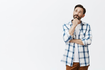 Charming and creative adult poet creating new poem while walking near lake, looking up with thoughtful expression, thinking, touching beard and holding hands crossed over gray background
