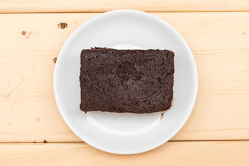 plain chocolate brownie in white plate on wooden plank. top view