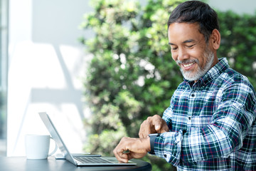 Smiling happy mature asian man with white stylish short beard using digital smartwatch and touching...