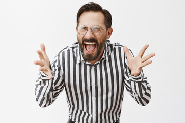 Fototapeta premium Man lost tempter in office, people scared to come near and calm him down. Displeased bothered and annoyed crazy man with dark short hair and beard, screaming with closed eyes and shaking hands