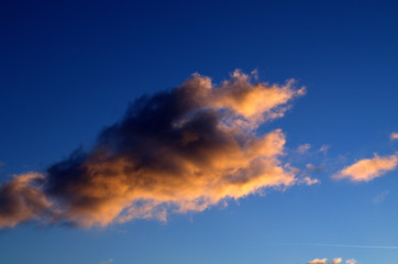 A single fluffy cloud is illuminated by the orange rays of the sun below. Dramatic landscape close-up on a blue sky