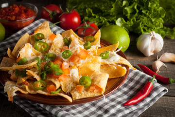 Mexican nachos with tortilla, hot pepper, melted cheese, ketchup and white sauce, jalapeno and lime on wooden background. Fast food and junk food concept. Chili con carne.