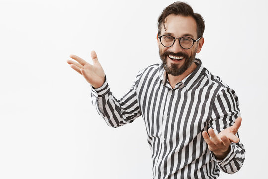 Tada. Portrait of charming confident and happy male entrepreneur in striped shirt and glasses, gesturing with palms in self-assured and friendly pose and smiling broadly, showing office to girlfriend