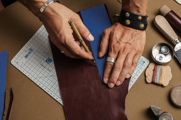 Tools and equipment for leather handmade goods. Cropped image of a male artisan making custom made wallet design for a new client at his workshop. Leathercraft, Small business, Handwork Concept.