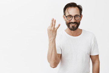 Man have three cars in garage, bragging about sucessful and rich life. Portrait of stylish good-looking mature male model in glasses with beard showing third number with fingers and smiling carefree