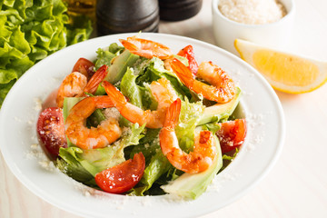 Fresh Caesar shrimp salad with delicious prawns, ruccola, spinach, cabbage, arugula, egg, parmesan and cherry tomato on wooden background. Oil, salt and pepper. Healthy and diet food concept.