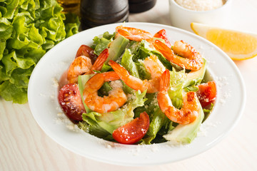 Fresh Caesar shrimp salad with delicious prawns, ruccola, spinach, cabbage, arugula, egg, parmesan and cherry tomato on wooden background. Oil, salt and pepper. Healthy and diet food concept.