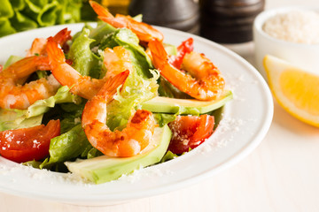 Fresh Caesar shrimp salad with delicious prawns, ruccola, spinach, cabbage, arugula, egg, parmesan and cherry tomato on wooden background. Oil, salt and pepper. Healthy and diet food concept.