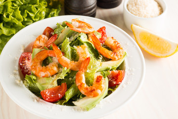 Fresh Caesar shrimp salad with delicious prawns, ruccola, spinach, cabbage, arugula, egg, parmesan and cherry tomato on wooden background. Oil, salt and pepper. Healthy and diet food concept.