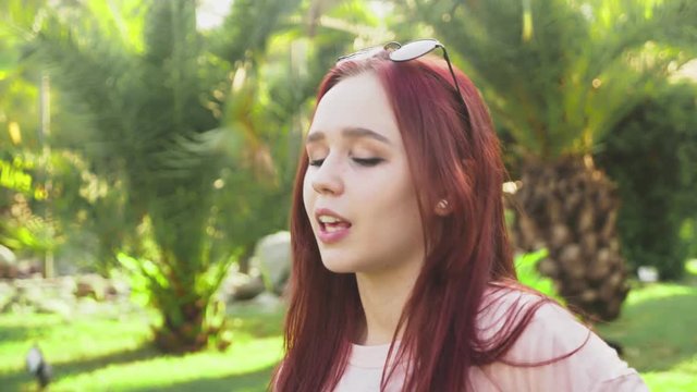 young beautiful red-haired girl dancing in the park. woman in a mini skirt dancing in a tropical park on a background of palms. 4k, slow motion