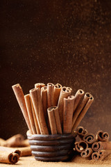Cinnamon sticks in bowl and powder on brown background. Aromatic spice.