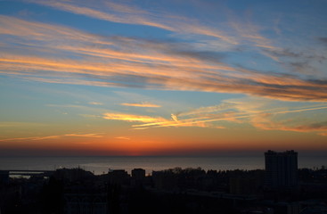 Dramatic yellow and orange clouds at sunset over the silhouette of the city and the sea