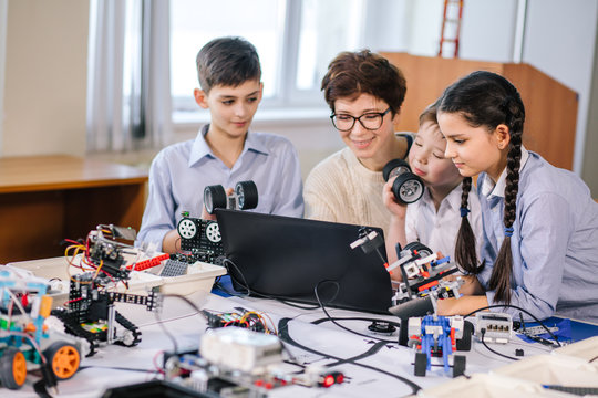 group of happy kids with their female adult science prof with tablet pc computer programming electric toys and robots at robotics hobby club