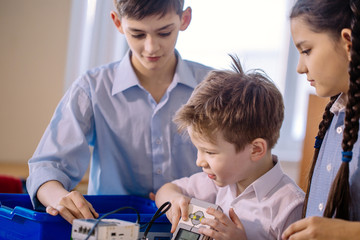 Little happy constructors kids playing with electrical robot while visiting robotics exhibition...
