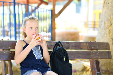 Little girl is eating an apple. Healthy nutrition. Pretty child eating an apple at park , nature outdoors. Teenager pupil enjoying healthy lunch in schoolyard.