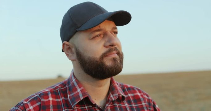 Close up of the good looking middle age Caucasian farmer in the hat looking at the horizon and thinking in the field. Portrait.