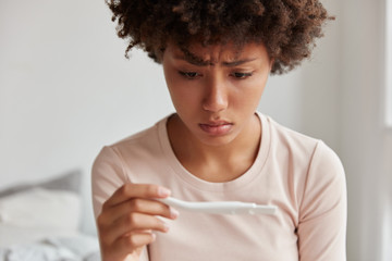 Desperate sad unhappy black woman looks at pregnancy test, being discontent with result, isnt ready...