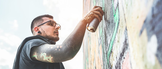 Tattooed graffiti writer painting with color spray his picture on the wall