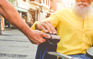 Male customer paying with contactless credit card with NFC technology - Waiter with a credit card reader machine at bar outdoor - New tech payment concept