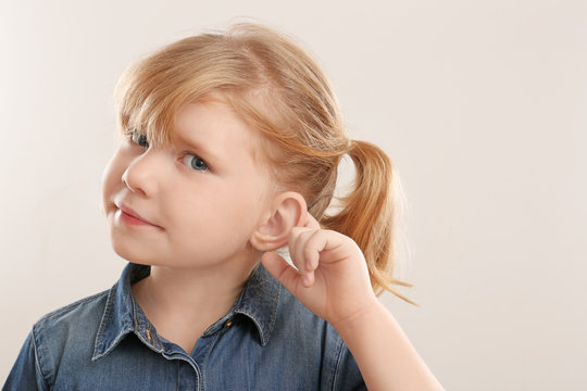 Cute little girl with hearing problem on light background