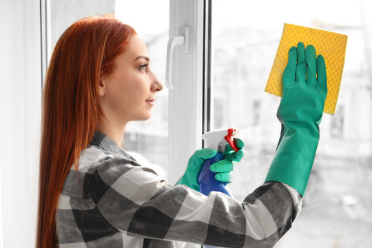 Young woman cleaning window indoors