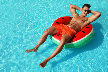 Young man with inflatable ring in pool on sunny day - Powered by Adobe