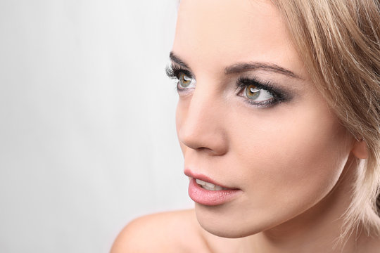 Portrait of beautiful young woman with eyelash extensions on light background
