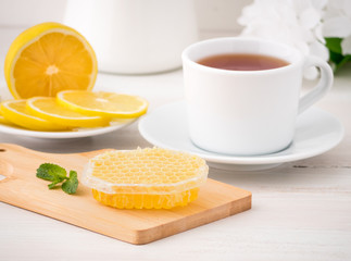White Cup with tea, lemon slices and honey in honeycomb on white wooden table, side view