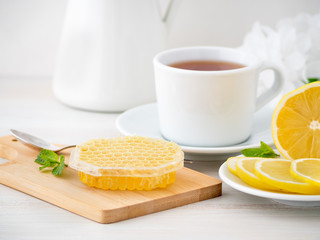 White Cup with tea, lemon slices and honey in honeycomb on white wooden table, side view