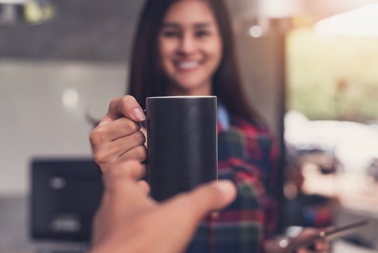 Smiling Asian business woman giving coffee to a colleague.