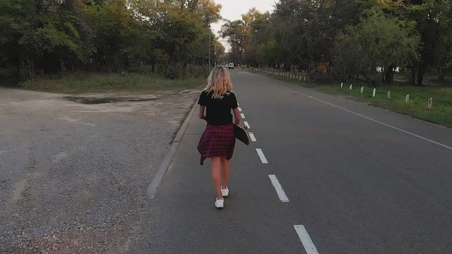 A young girl in white shorts and a black T-shirt is riding on a skateboard at sunset in the evening. Sunset. Sports and fitness. Slow motion. Aerial Filming