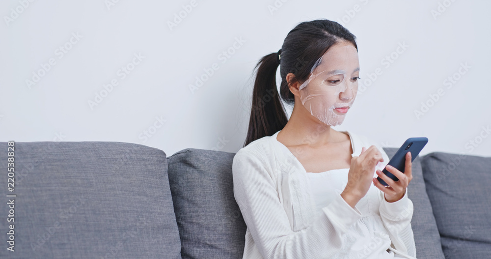 Wall mural Woman apply paper mask on face and use of mobile phone